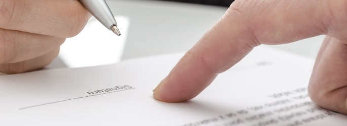 Detail of a woman signing a paper. Male finger showing where to sign.