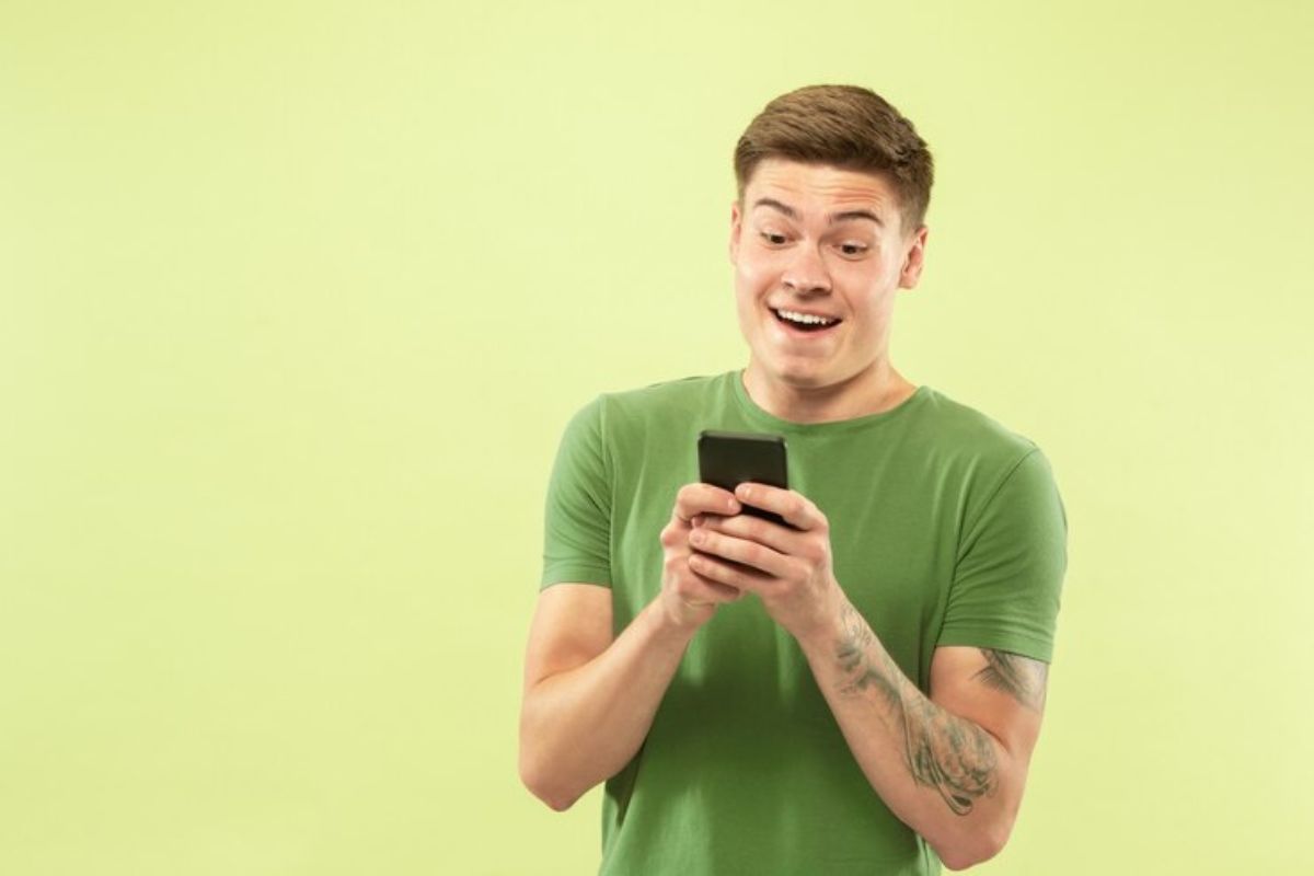 Um homem de camisa verde olha atentamente para o seu celular