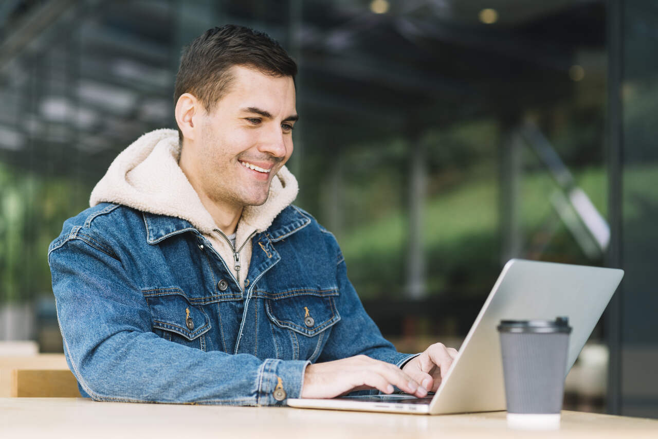 Jovem sorri enquanto faz algo em seu notebook 