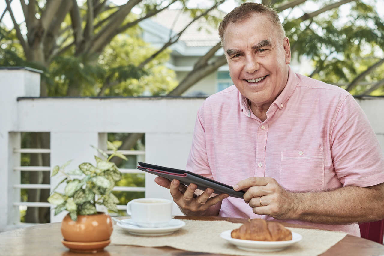 Homem adulto tomando café e mexendo em seu tablet 