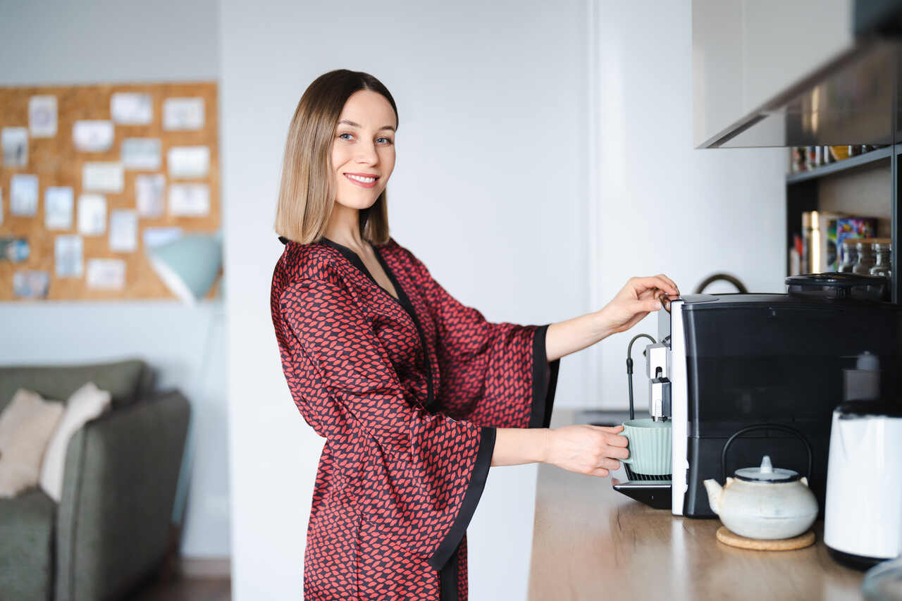 Mulher posa sorridente enquanto serve café da cafeteira 