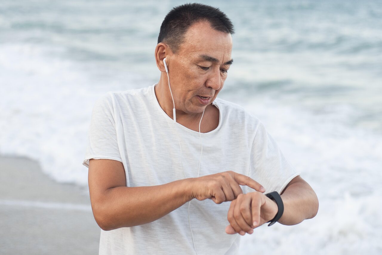 Homem adulto correndo na praia enquanto confere smartwatch no pulso