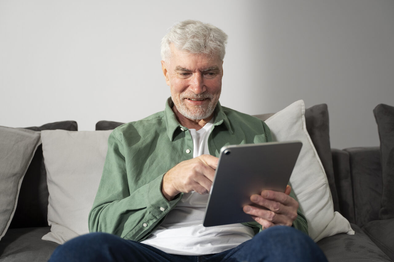 Idoso sentado no sofá mexendo em seu tablet