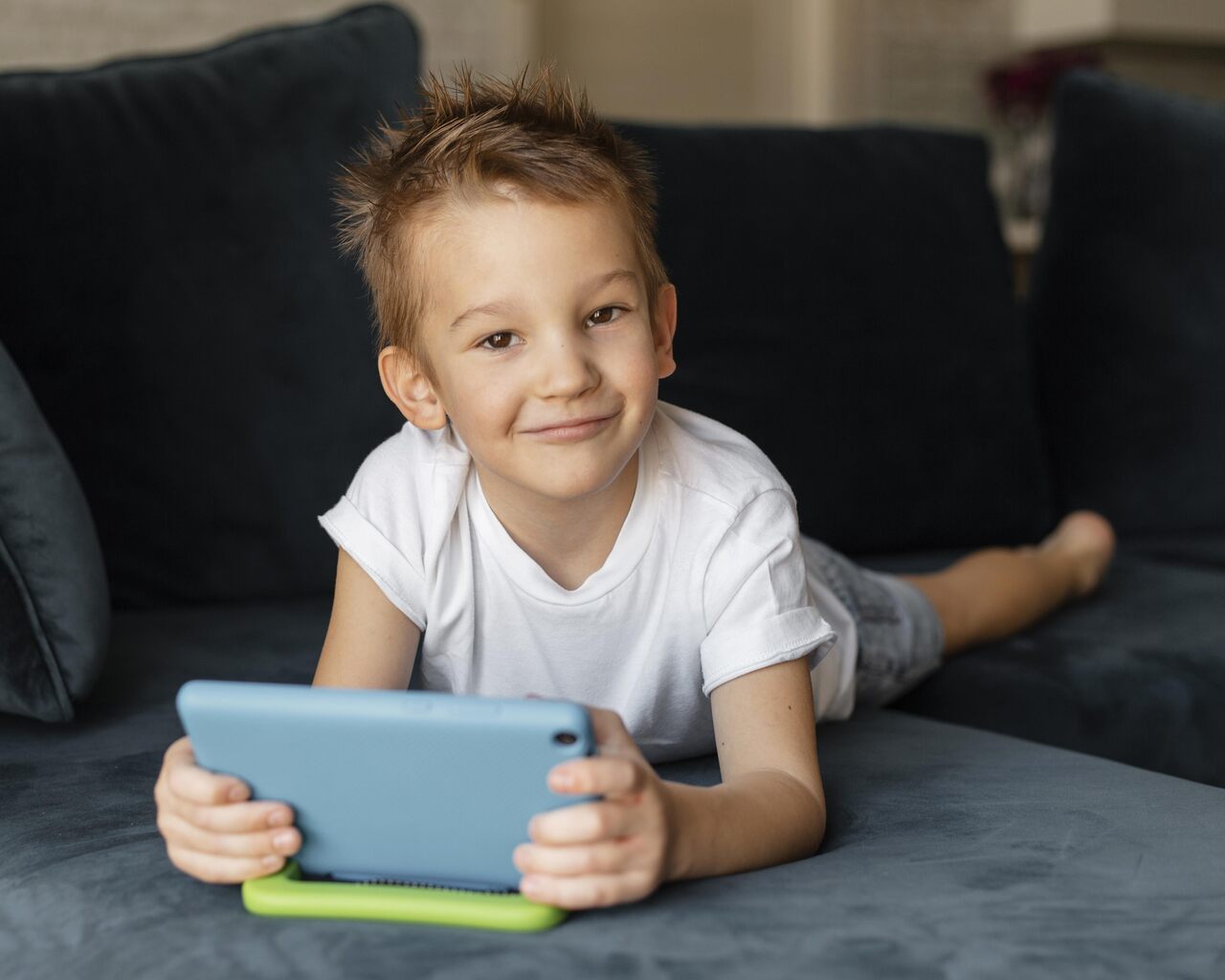 Criança brinca com tablet deitada na cama 