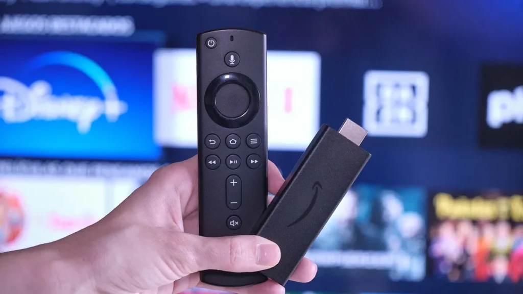 Pessoa segurando um Fire Stick Amazon na mão em frente a uma televisão